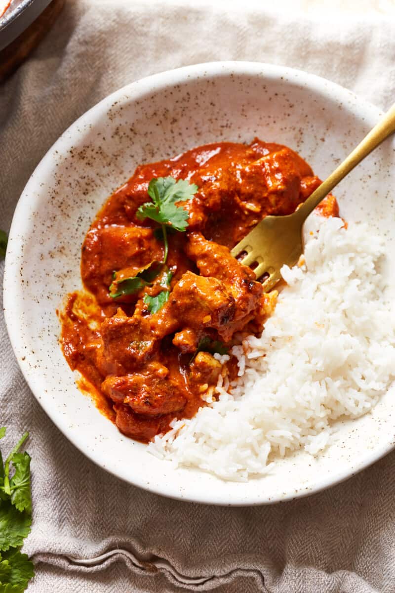 white bowl with chicken tikka masala and rice with cilantro