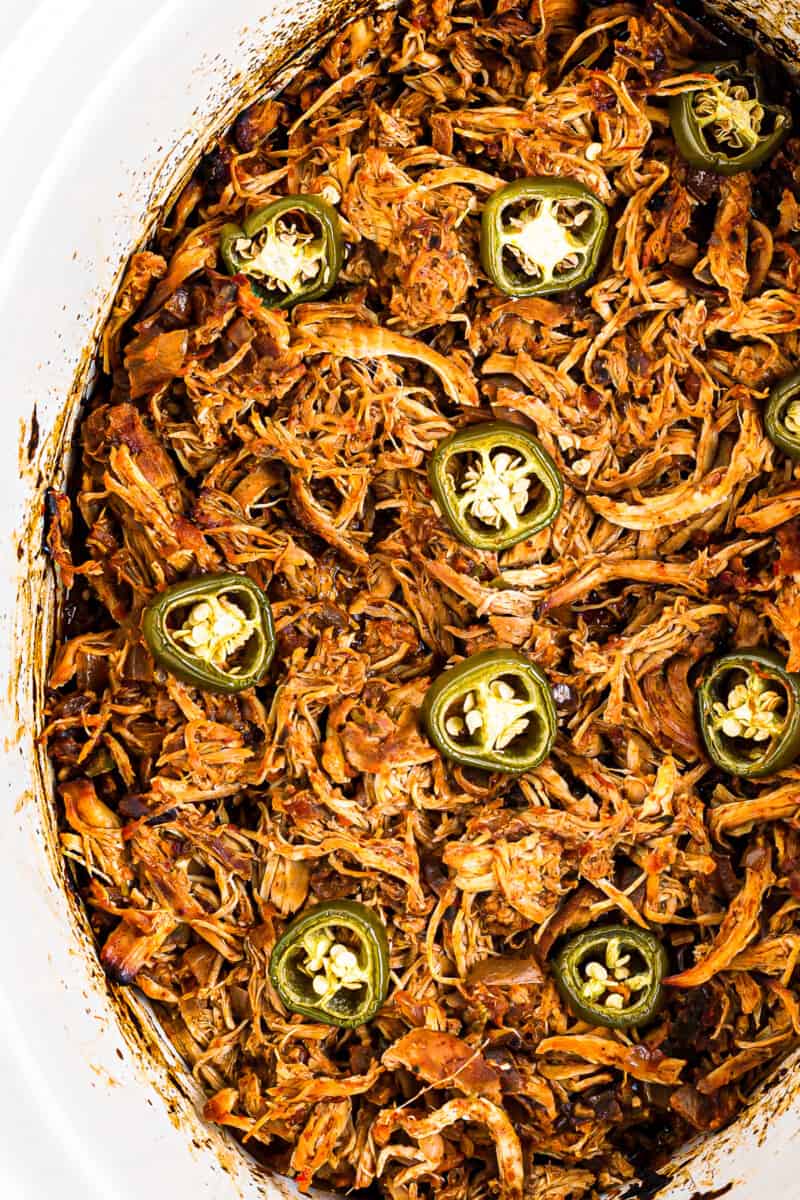 shredded salsa chicken in a crockpot topped with sliced jalapenos