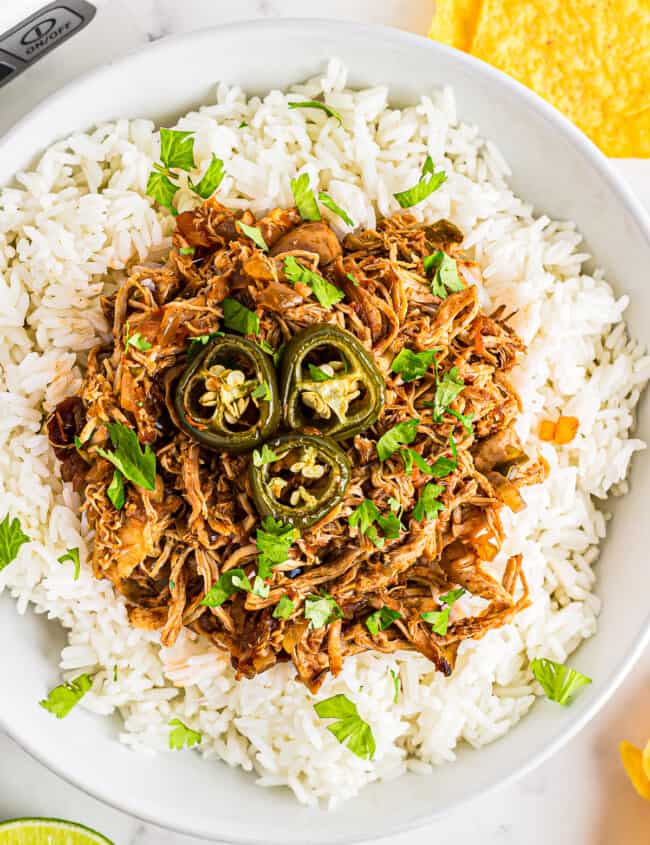 overhead image of shredded salsa chicken and rice topped with jalapeno slices in a white bowl