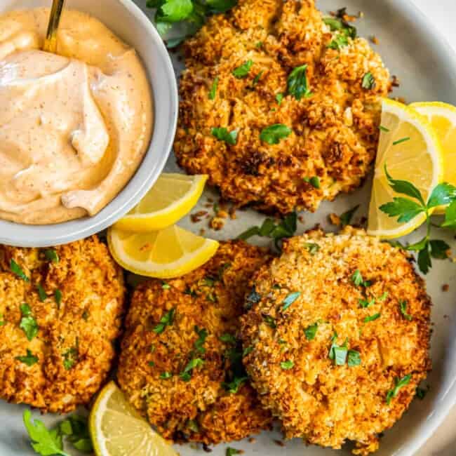 crab cakes on a plate with lemon slices and sauce in a bowl with a spoon