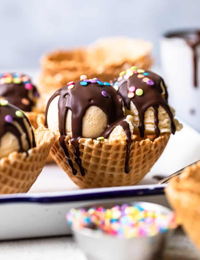 scoops of ice cream in waffle cone bowls topped with chocolate magic shell and sprinkles
