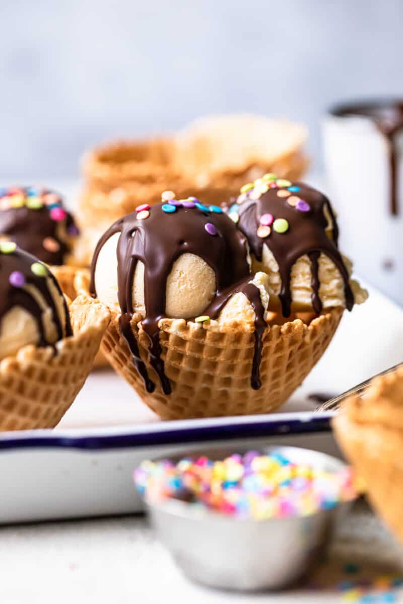 scoops of ice cream in waffle cone bowls topped with chocolate magic shell and sprinkles