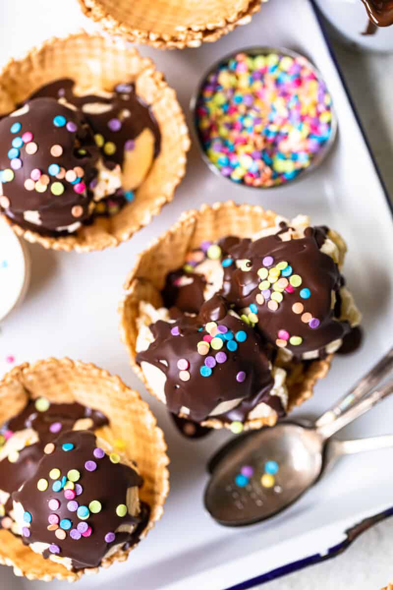 overhead image of scoops of ice cream in waffle cone bowls topped with chocolate magic shell and sprinkles