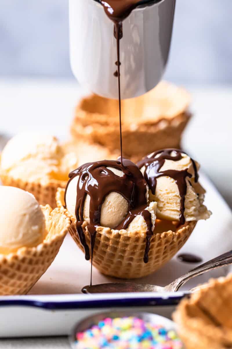 pouring chocolate magic shell topping onto ice cream scoops in a waffle cone bowl