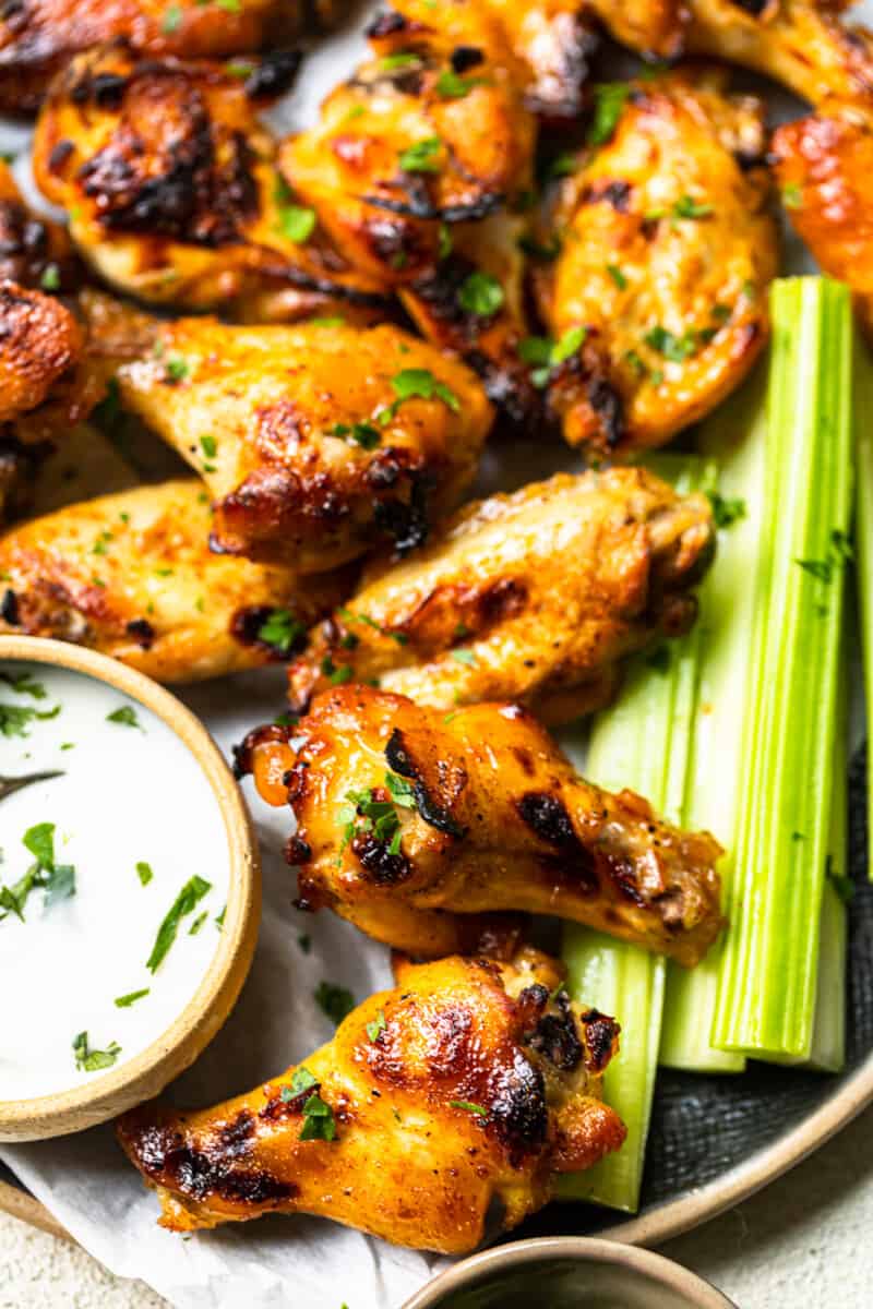 hot honey chicken wings and celery slices on a serving tray with ranch dip in a small bowl with a spoon