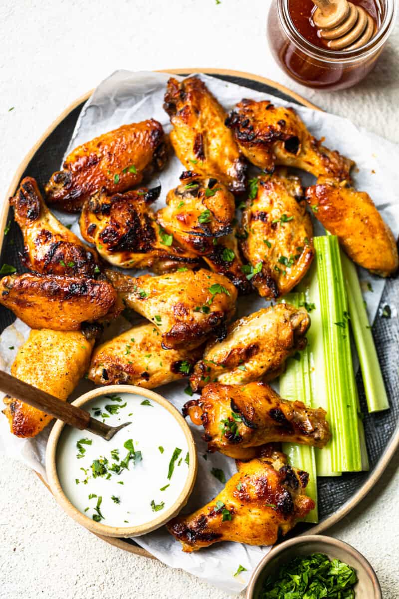 overhead image of hot honey chicken wings and celery slices on a serving tray with ranch dip in a small bowl with a spoon