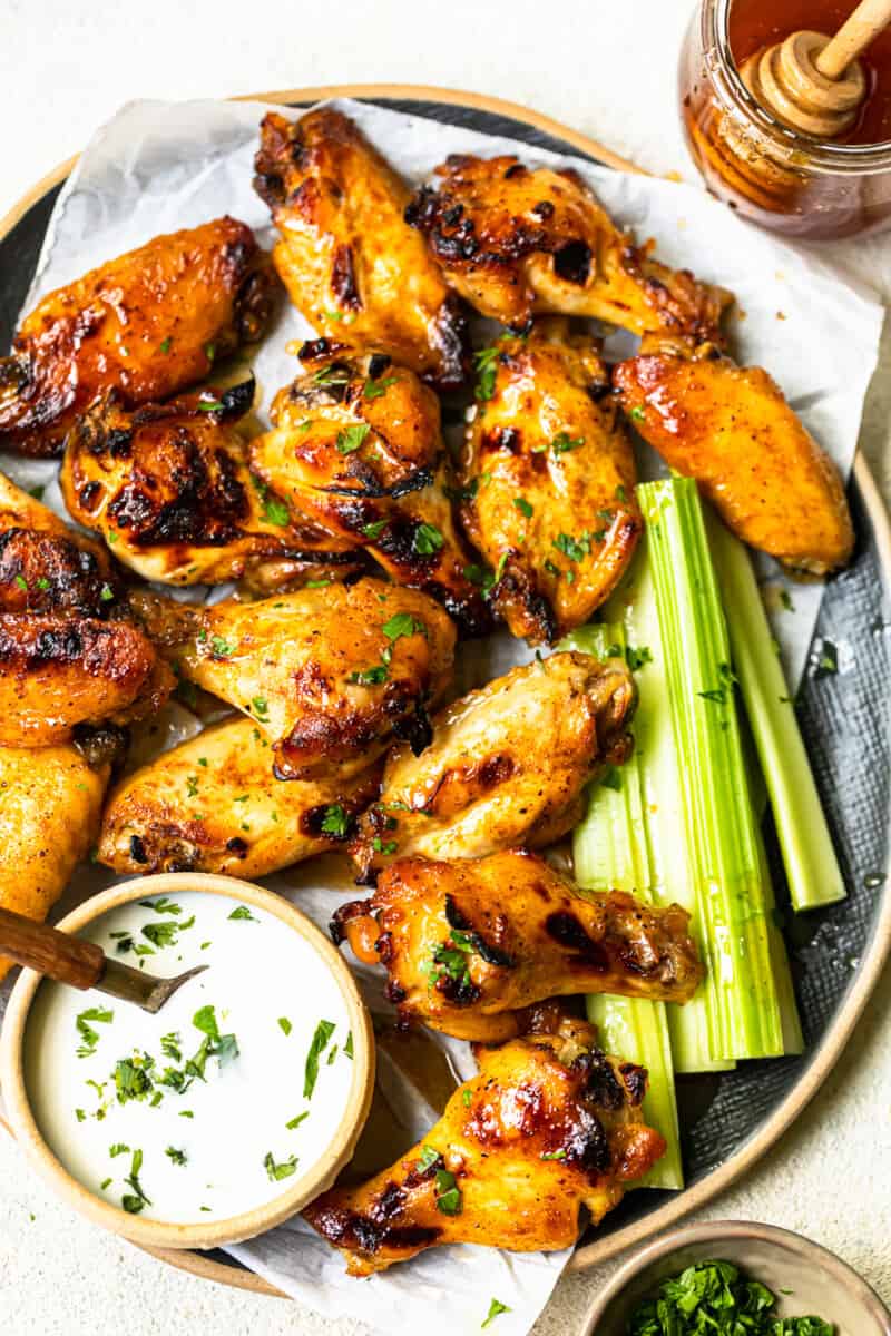 overhead image of hot honey chicken wings and celery slices on a serving tray with ranch dip in a small bowl with a spoon