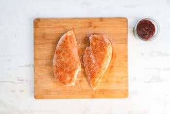 2 chicken breasts with spice rub on a wood cutting board