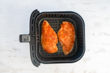 2 chicken breasts in air fryer basket before cooking