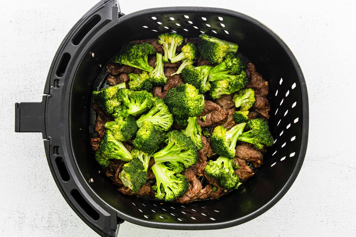 broccoli florets on top of cooked steak slices in air fryer basket