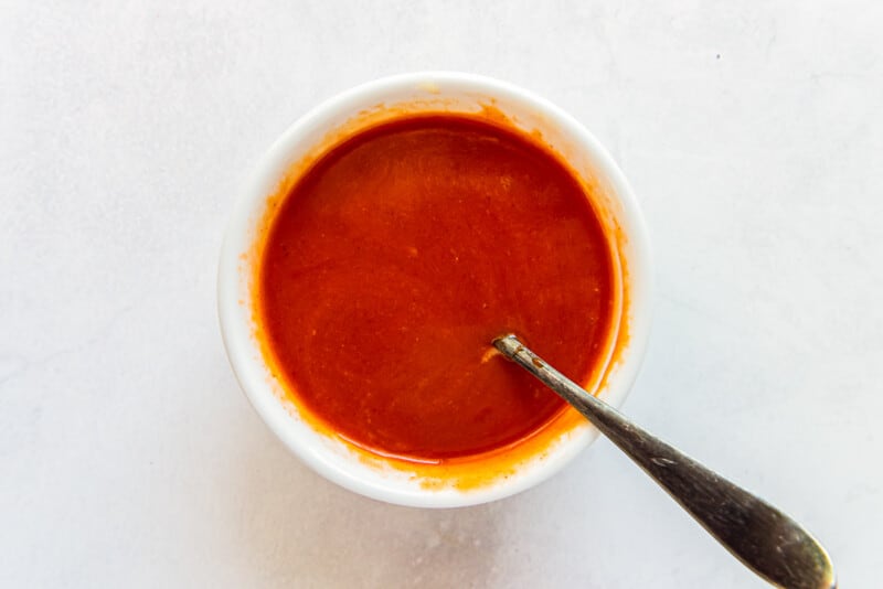 Buffalo sauce and melted butter in a white bowl with a spoon