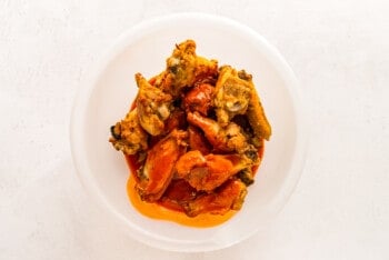 cooked chicken wings in a bowl with Buffalo sauce mixture