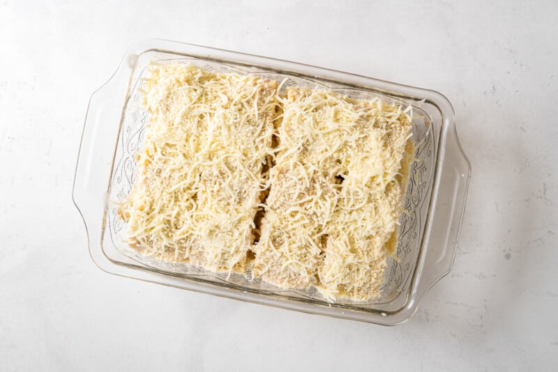 chicken alfredo lasagna roll ups topped with alfredo sauce and shredded cheese in a casserole dish before baking