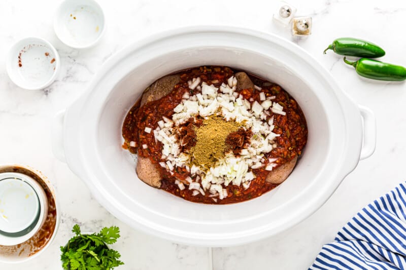 spices and salsa on top of chicken breasts in a slow cooker