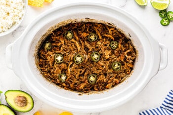 shredded salsa chicken topped with sliced jalapenos in a crockpot