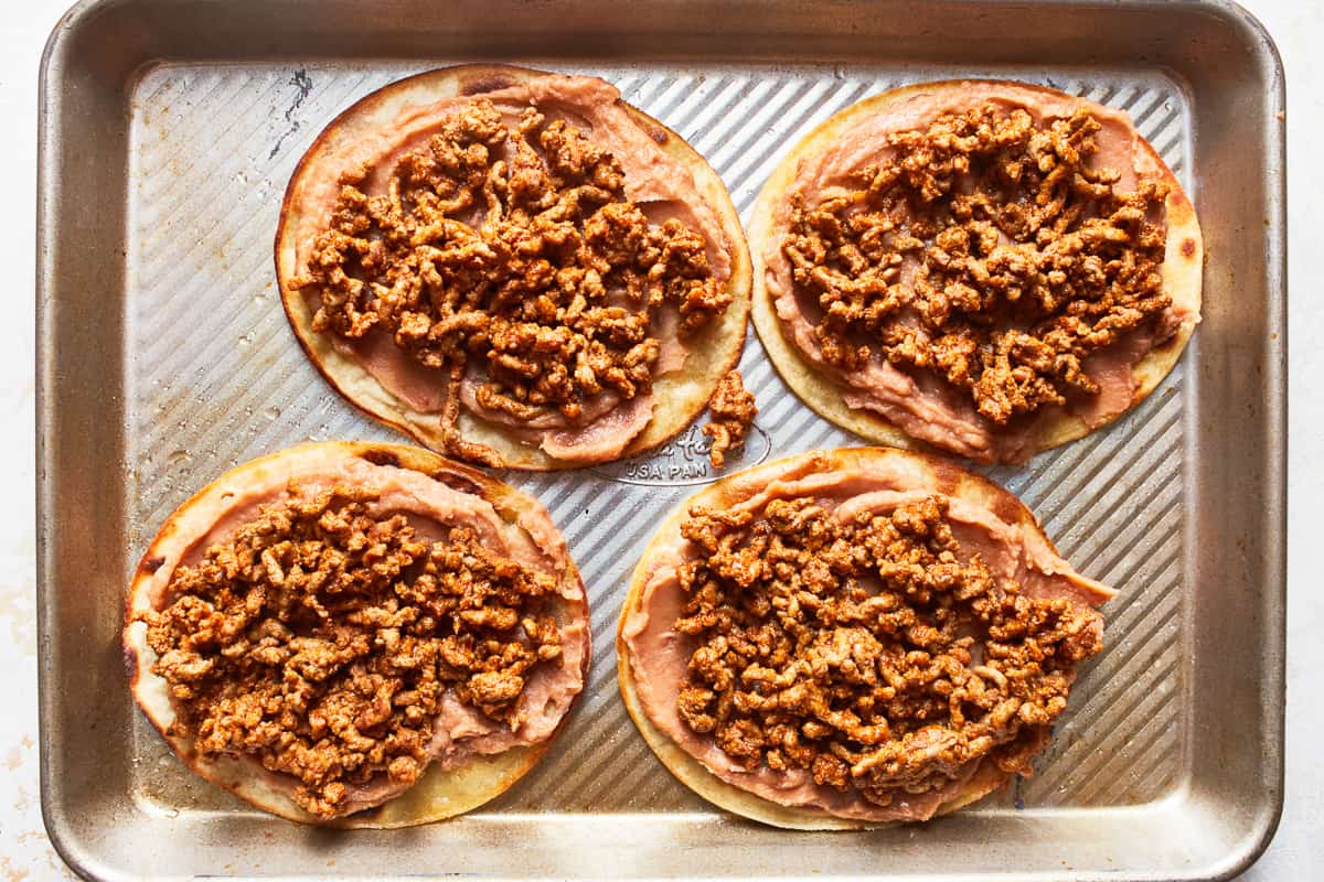 Beef and beans on top of tortillas on a baking sheet.  - 9