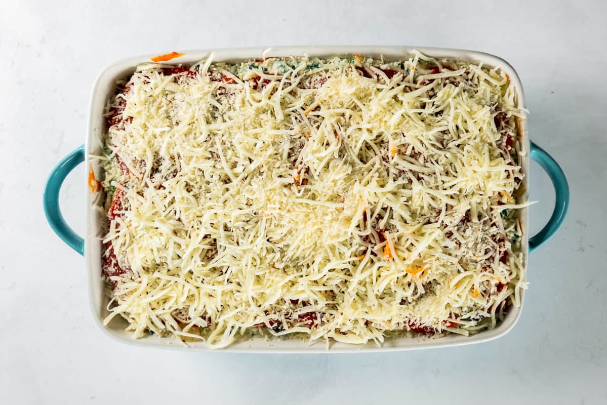 shredded cheese sprinkled on top of lasagna layers in a baking dish
