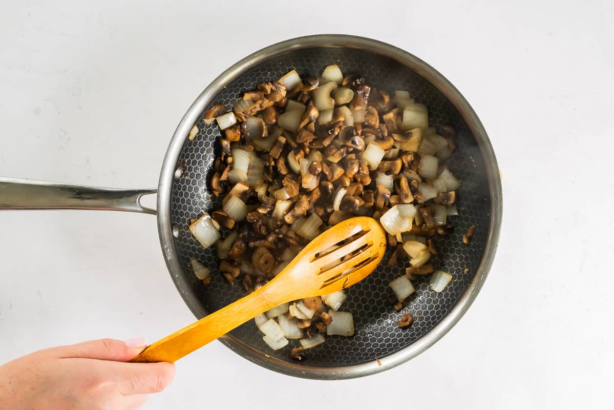 sautéed mushrooms, onion, and garlic in a skillet with a wood spoon