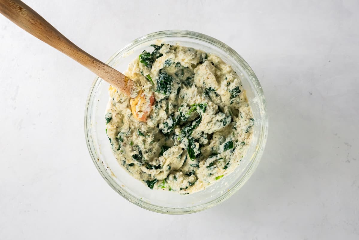 spinach ricotta mixture in a glass bowl with a wood spoon