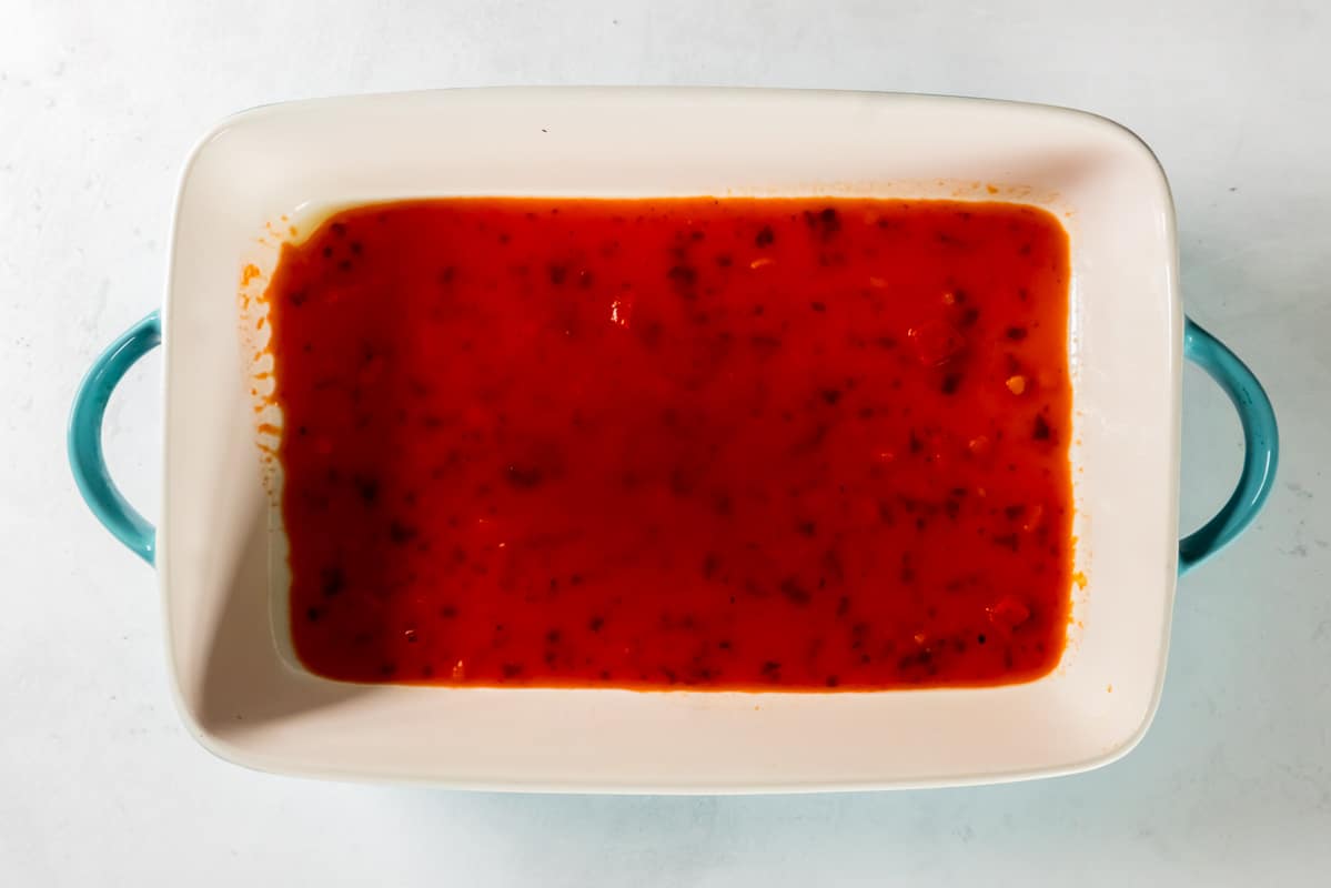 Layer of marinara sauce spread on the bottom of a baking dish. - 11