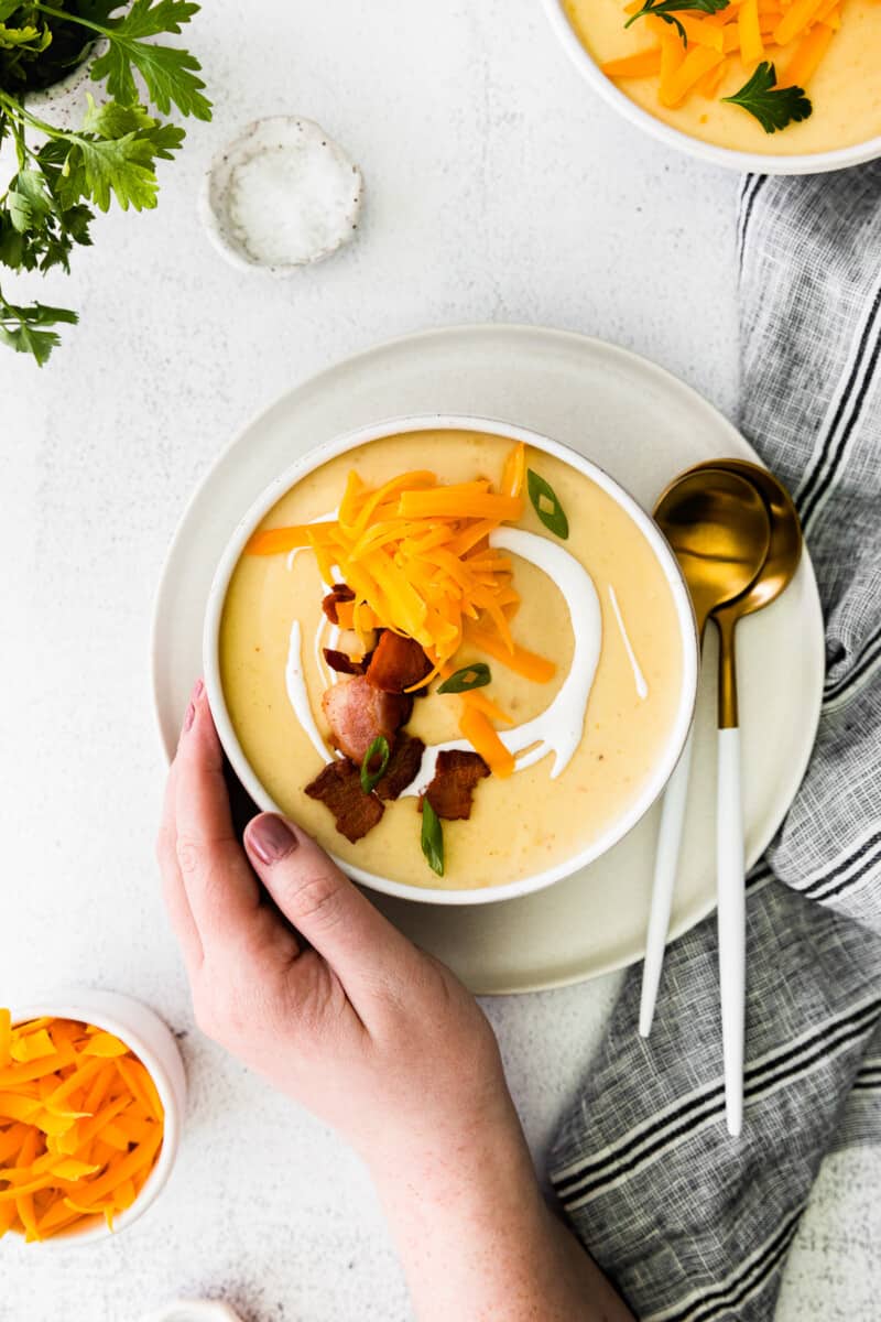 hand holding a bowl of potato soup topped with shredded cheddar cheese and bacon