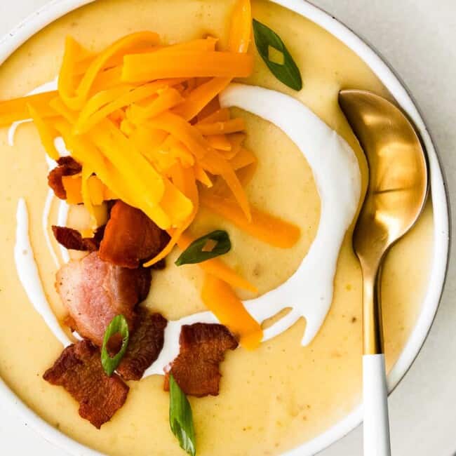 overhead image of creamy potato soup in a white bowl topped with shredded cheddar cheese and bacon with a spoon