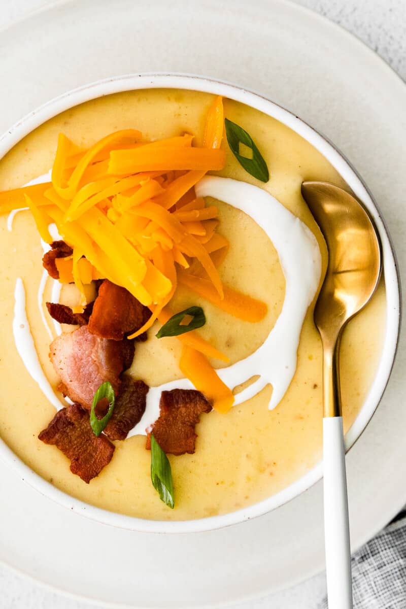 overhead image of creamy potato soup in a white bowl topped with shredded cheddar cheese and bacon with a spoon