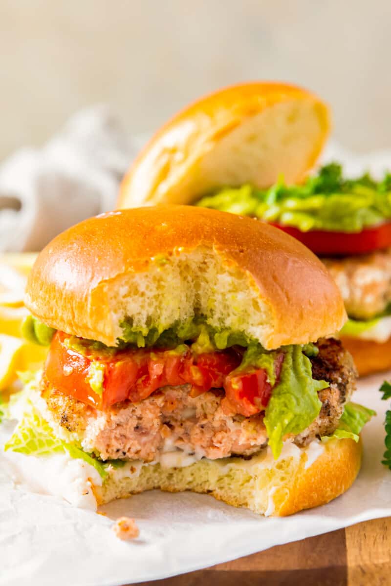 salmon burger on a bun with lettuce and tomato with a bite taken from it