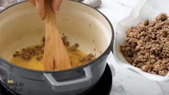 a wooden spatula removing ground beef from a dutch oven and adding it to a plate lined with paper towels.