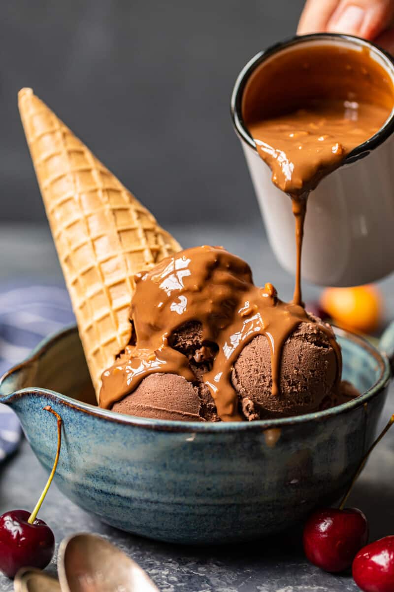 pouring symphony bar chocolate shell onto scoops of chocolate ice cream in a blue bowl