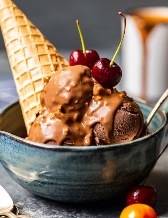 chocolate ice cream scoops topped with symphony bar chocolate shell and cherries in a blue bowl with a spoon