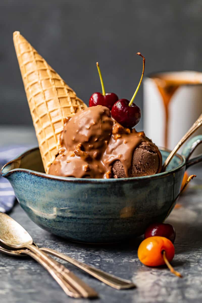 chocolate ice cream scoops topped with symphony bar chocolate shell and cherries in a blue bowl with a spoon