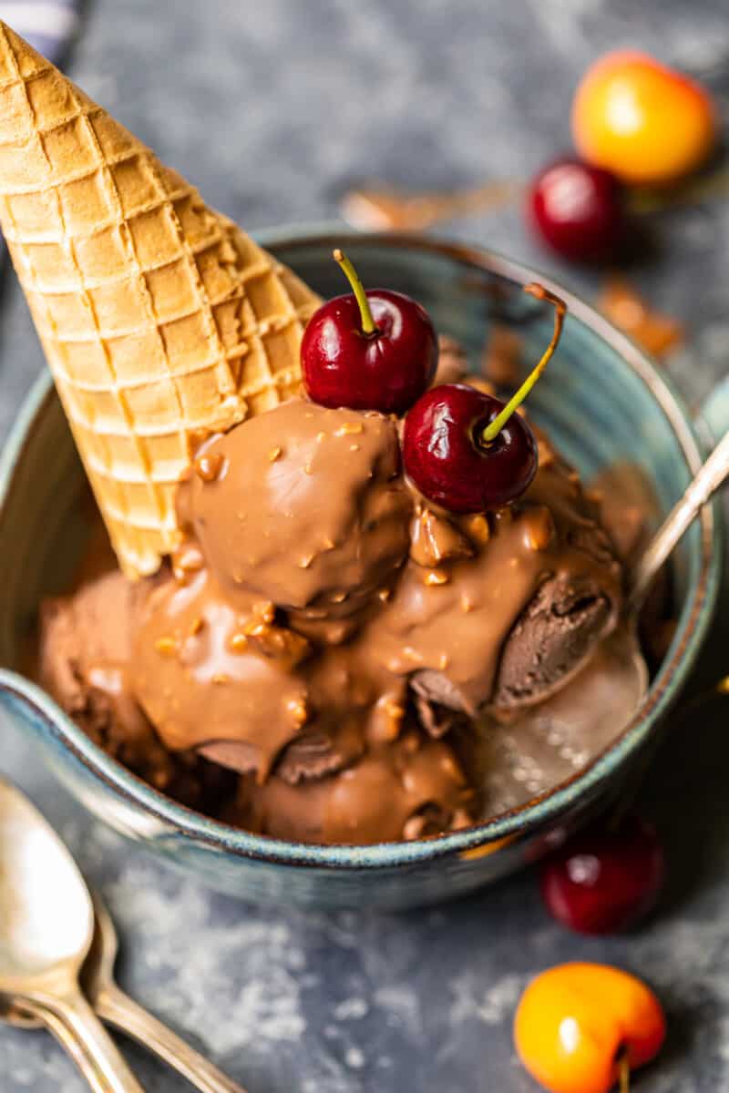 chocolate ice cream scoops topped with symphony bar chocolate shell and cherries in a blue bowl with a spoon