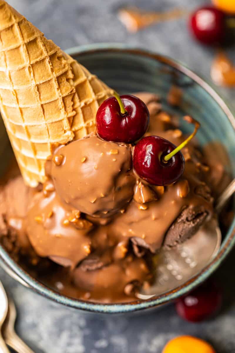 chocolate ice cream scoops topped with symphony bar chocolate shell and cherries in a blue bowl with a spoon