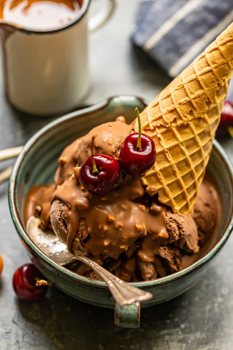 chocolate ice cream scoops topped with symphony bar chocolate shell and cherries in a blue bowl with a spoon