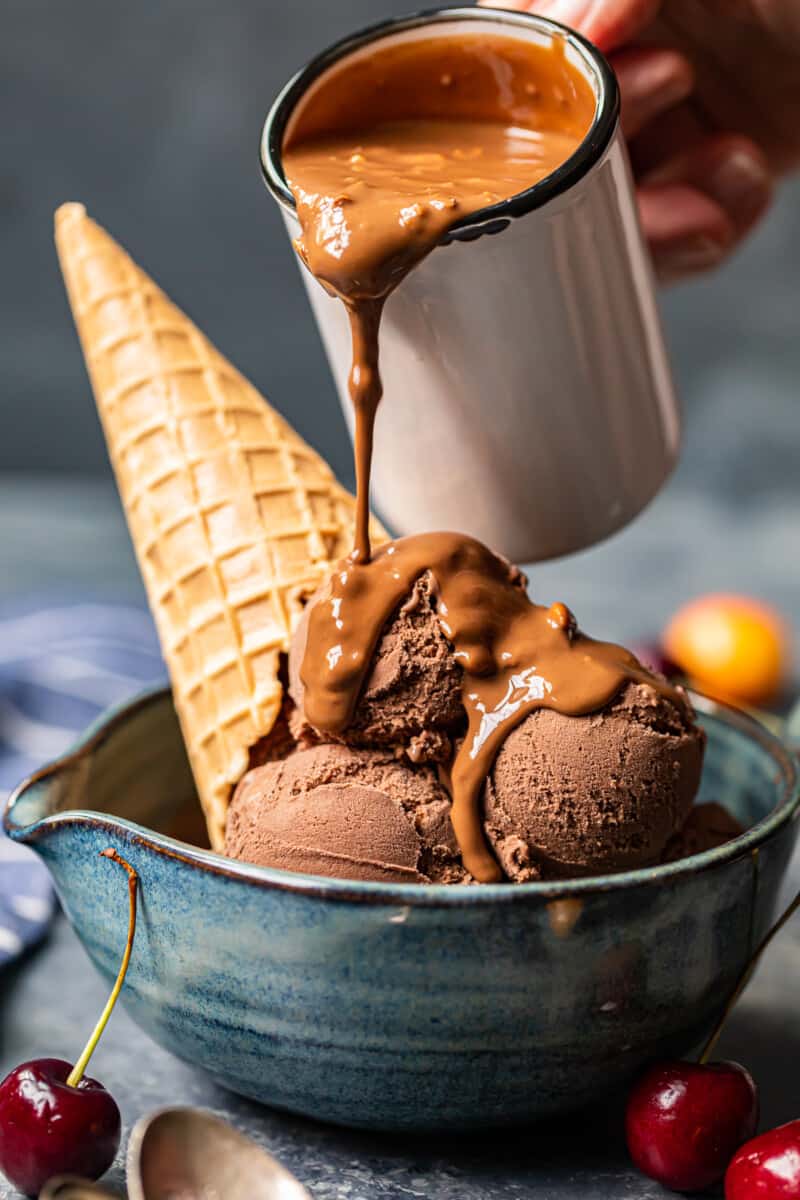 pouring symphony bar chocolate shell onto scoops of chocolate ice cream in a blue bowl