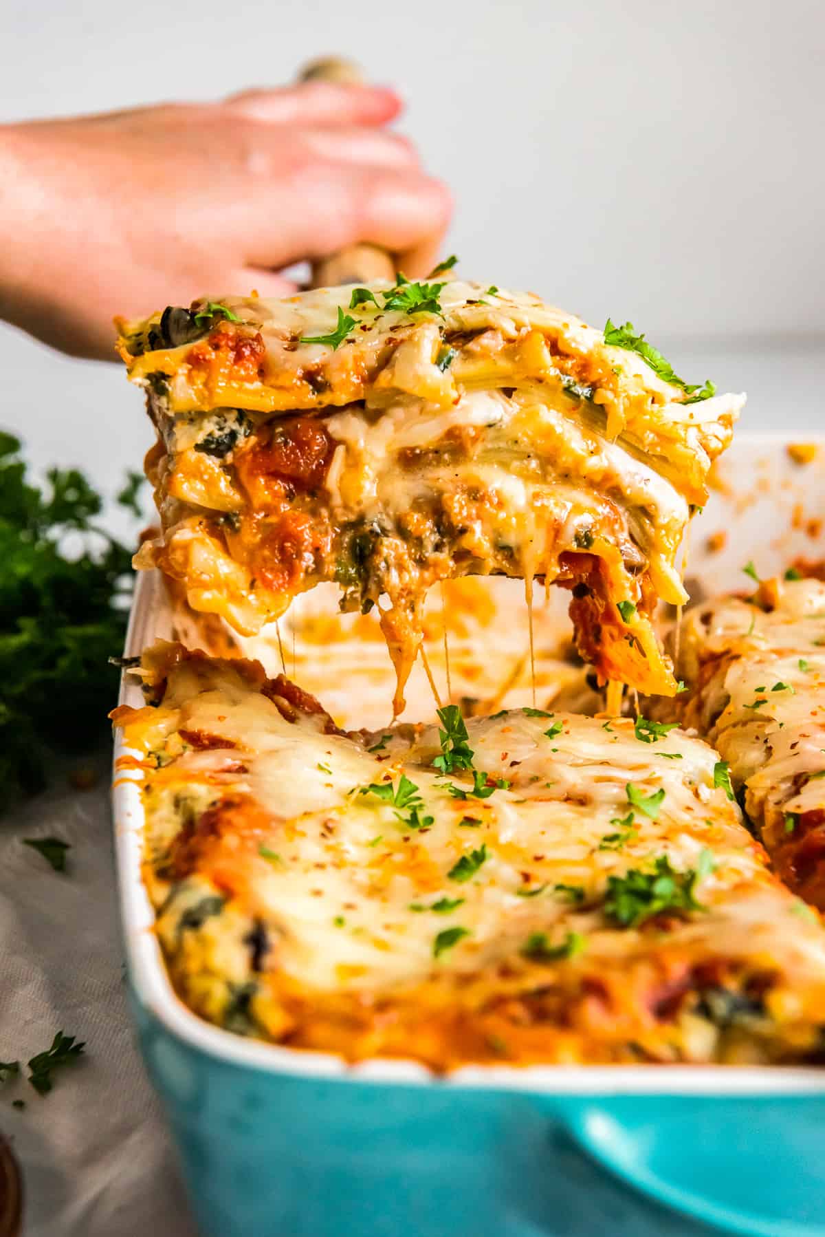 hand removing a slice of vegetarian lasagna from the baking dish with a spatula