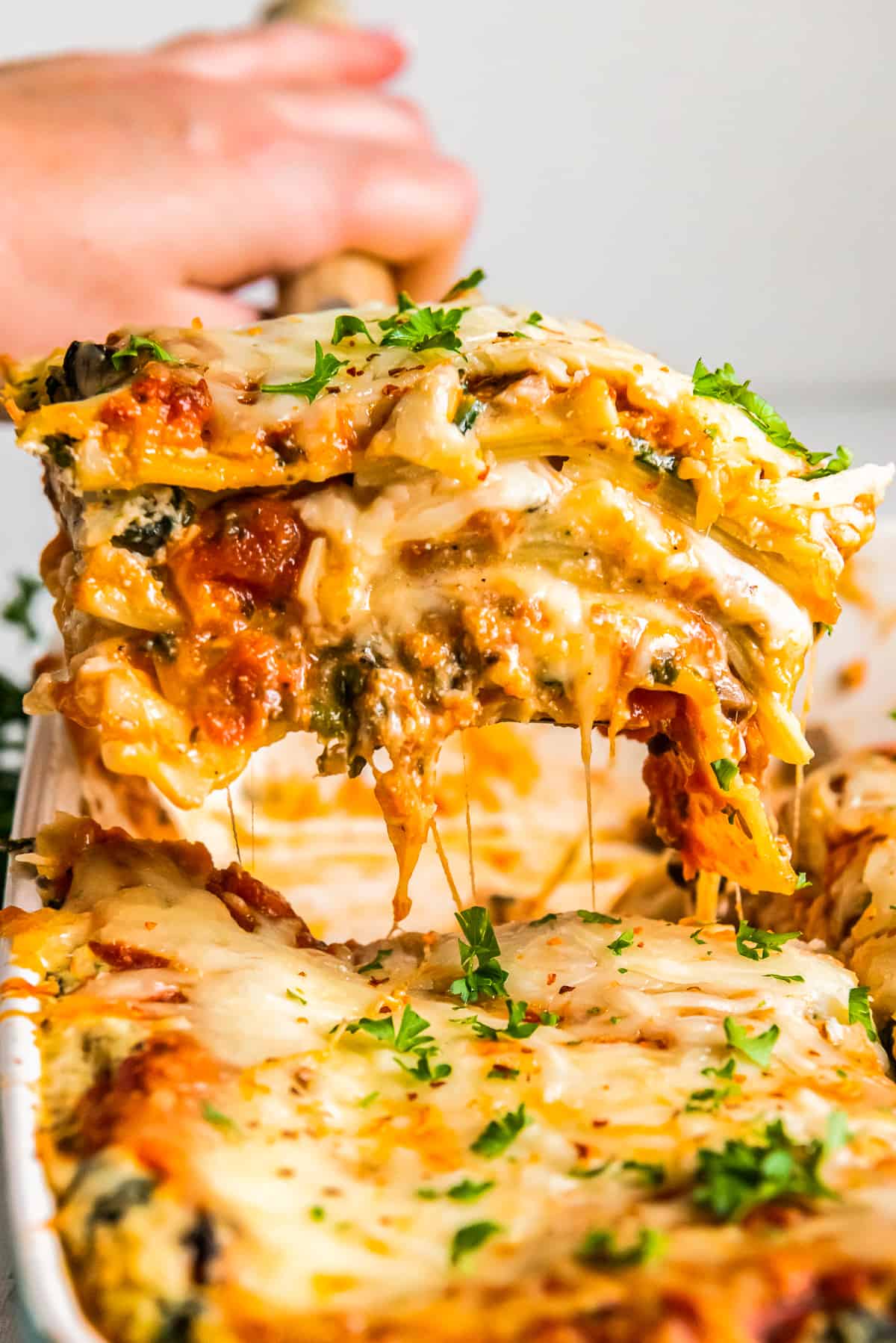 hand removing a slice of vegetarian lasagna from the baking dish with a spatula