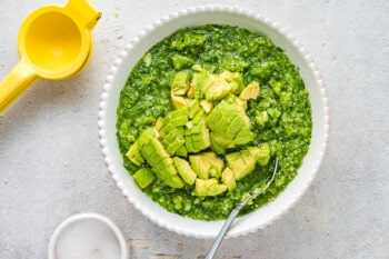 diced avocado added to tomatillo salsa in a white bowl with a spoon