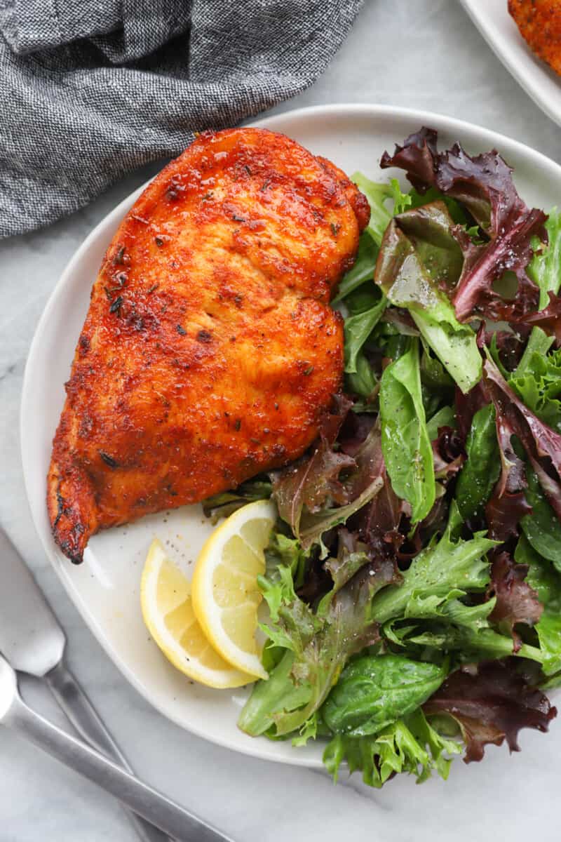 chicken breast on a white plate with salad