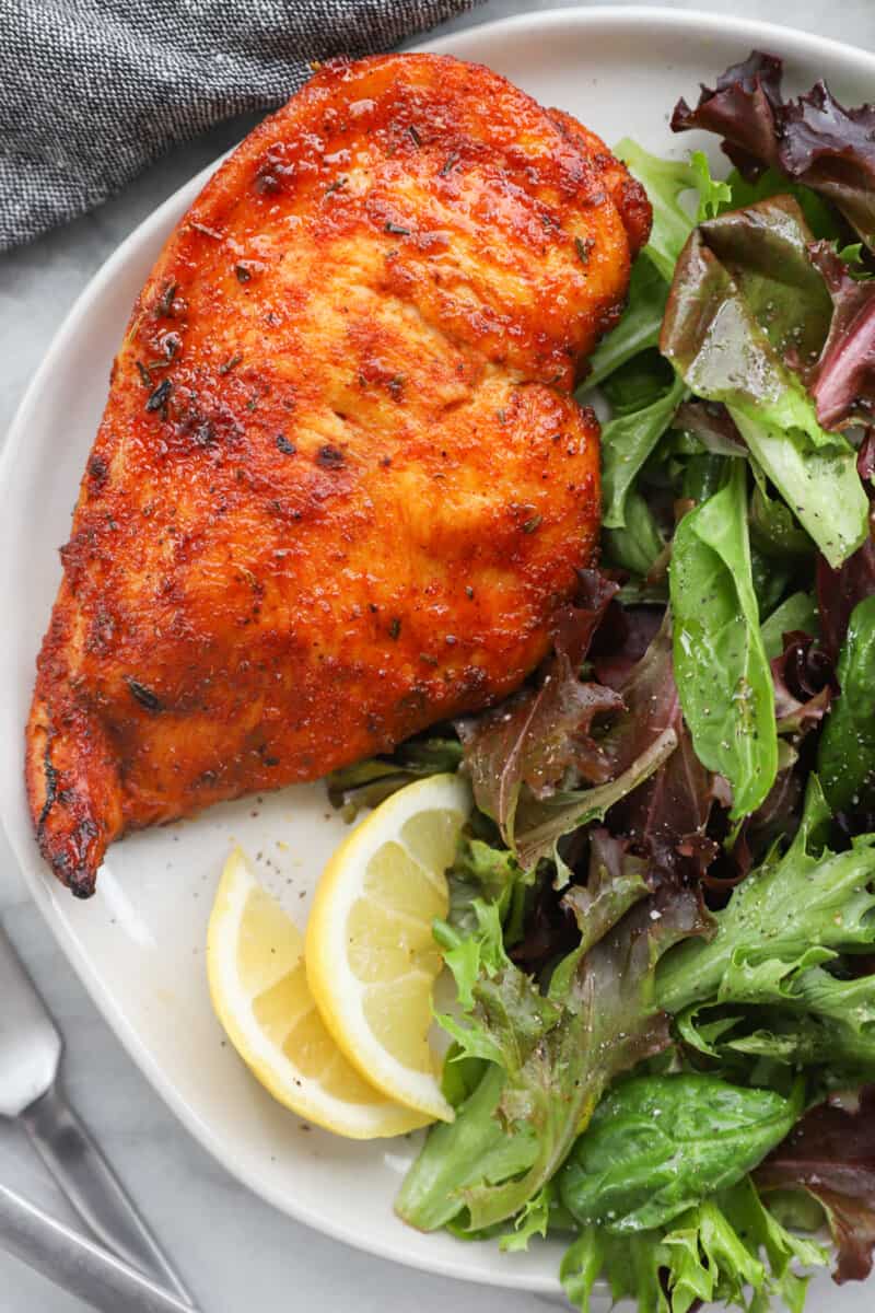 chicken breast on a white plate with salad