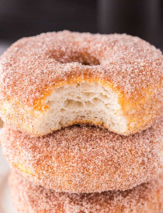 stack of 3 cinnamon sugar donuts with a bite taken from the top one