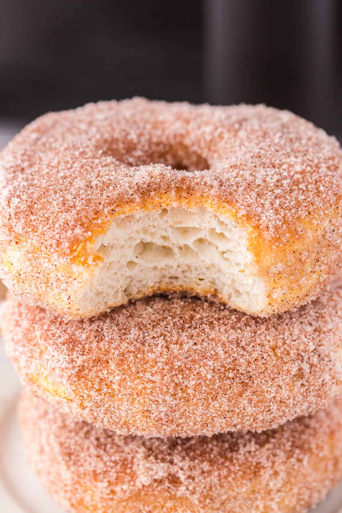 stack of 3 cinnamon sugar donuts with a bite taken from the top one