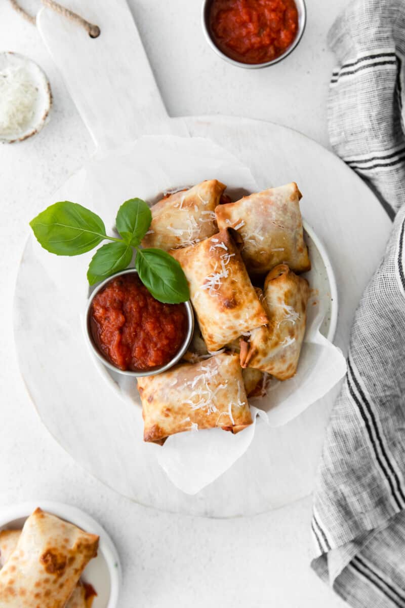 overhead image of pizza rolls in a white bowl with pizza sauce in a metal bowl