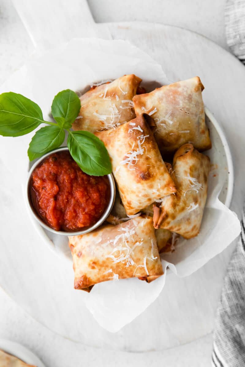 overhead image of pizza rolls in a white bowl with pizza sauce in a metal bowl