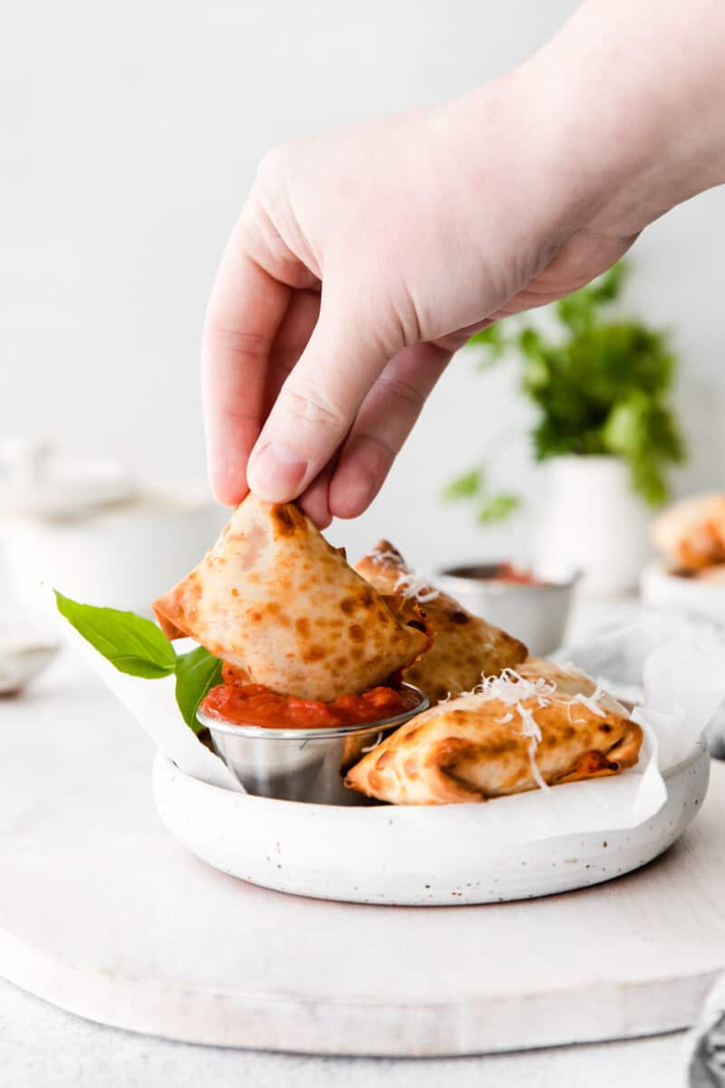 hand dipping a pizza roll into a bowl of pizza sauce