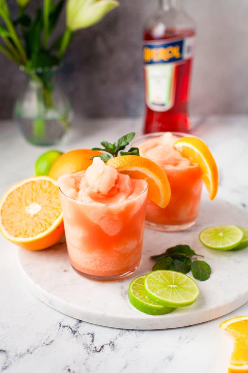 frozen Aperol margaritas in glasses with orange slice and mint garnishes