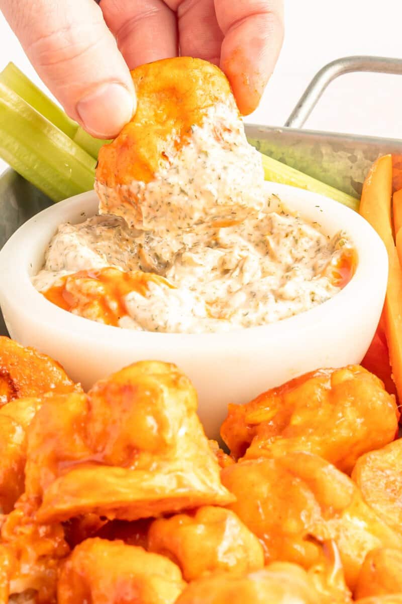 hand dipping a buffalo cauliflower wing into a bowl of buffalo ranch dressing