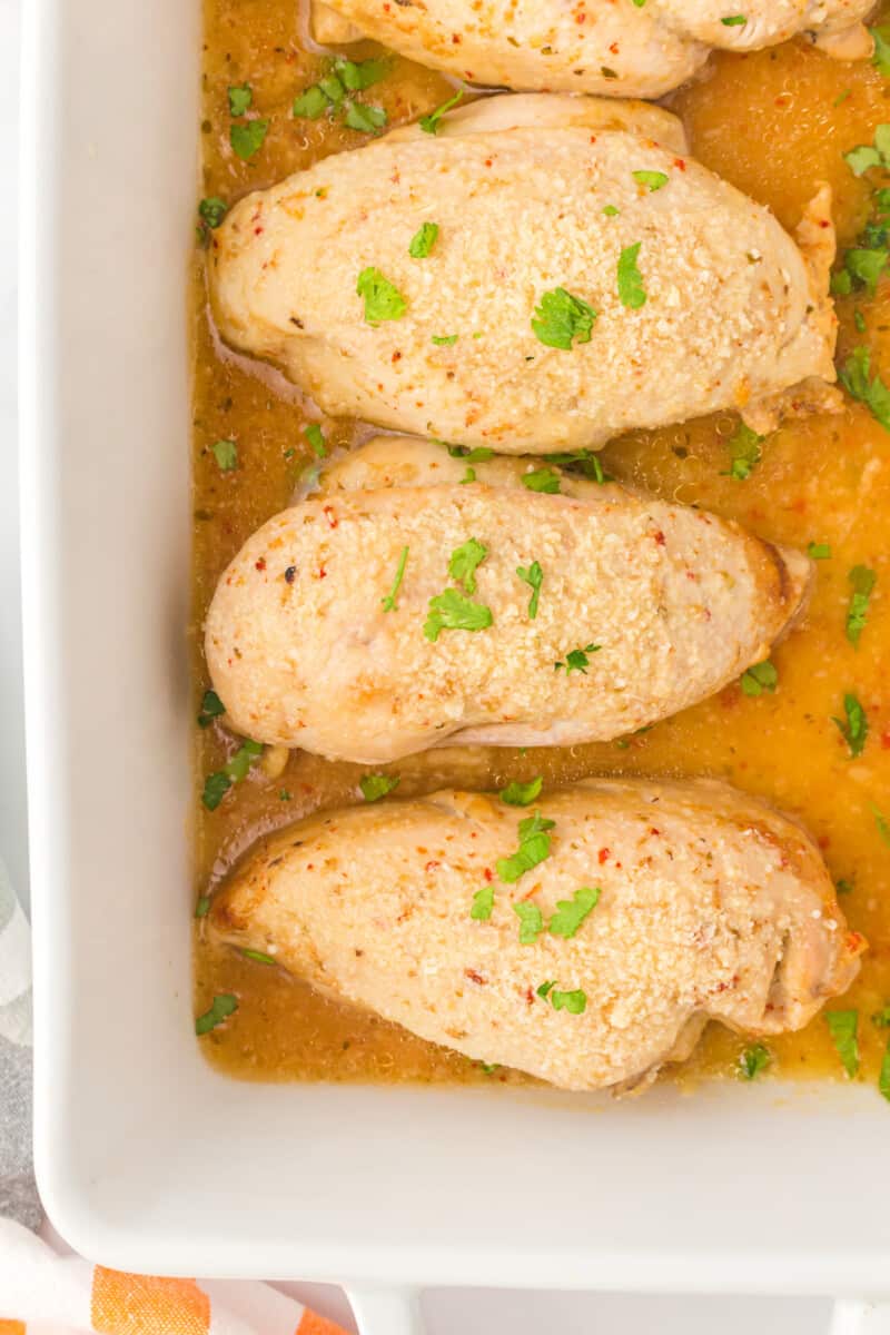 overhead image of baked Italian chicken breasts in a white baking dish