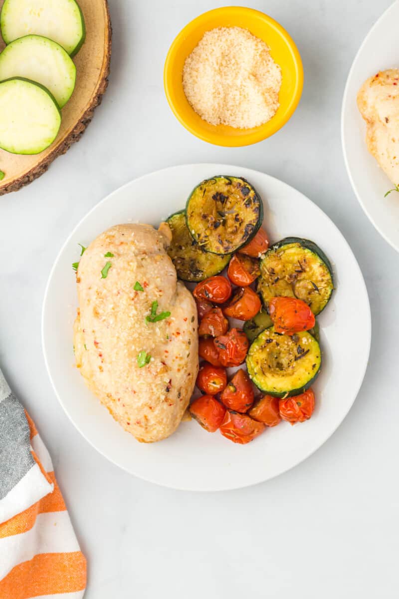 overhead image of Italian chicken breast on a white plate with roasted vegetables